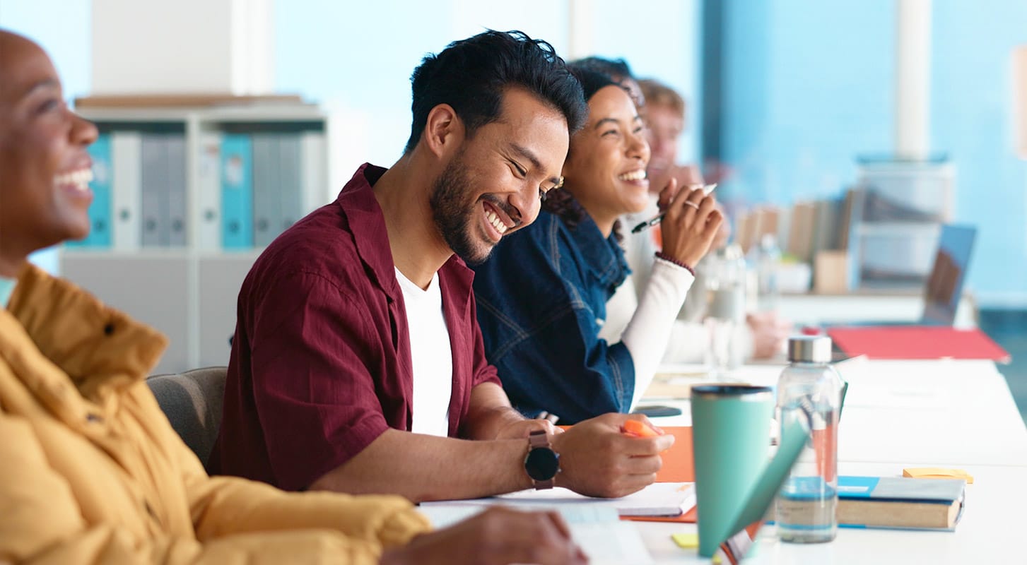 A group of diverse individuals seated at a table smiling, engaged in discussion or collaboration.
